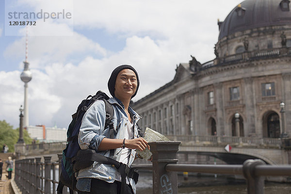 Lächelnder junger männlicher Tourist mit Karte am Geländer gegen das Bode-Museum  Berlin  Deutschland