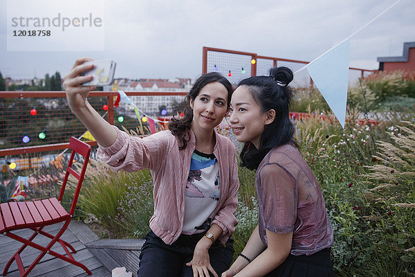 Lächelnde Frauen nehmen Selfie mit Smartphone auf der Terrasse