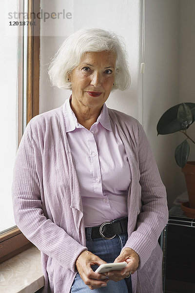 Porträt einer älteren Frau mit Handy auf der Fensterbank im Büro