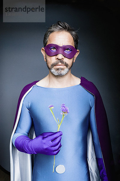Porträt eines als Superhelden gekleideten Mannes mit Blume auf grauem Hintergrund