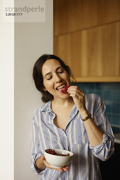 Junge Frau isst rote Johannisbeeren zu Hause