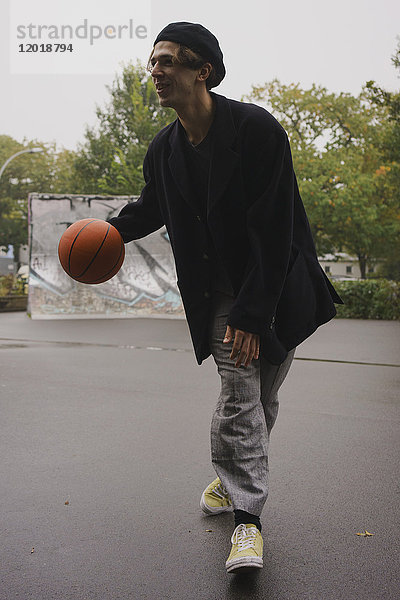 Junger Mann spielt Basketball im Park