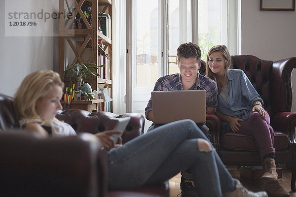 Frau mit digitalem Tablett  während Freunde den Laptop zu Hause benutzen