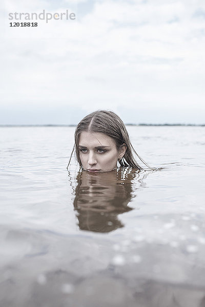 Nachdenkliche junge Frau  die im See gegen den Himmel schwimmt.