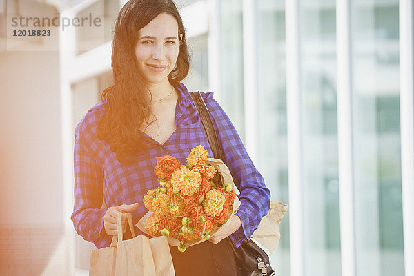 Porträt einer lächelnden Frau  die einen Blumenstrauß gegen das Gebäude hält.