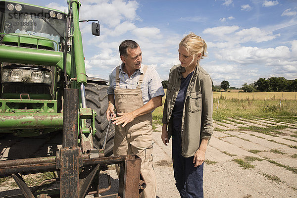 Mann  der die Frau erklärt  während er auf dem Bauernhof an einer Landmaschine steht.