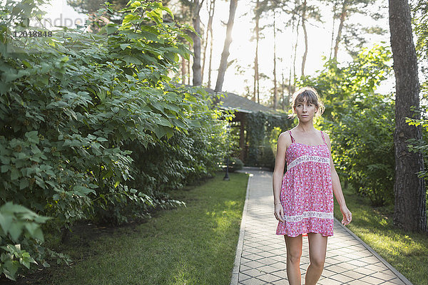 Frau in rosa Kleid auf dem Weg inmitten von Pflanzen im Hof