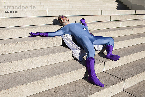 Mann als Superheld verkleidet auf einer Treppe liegend