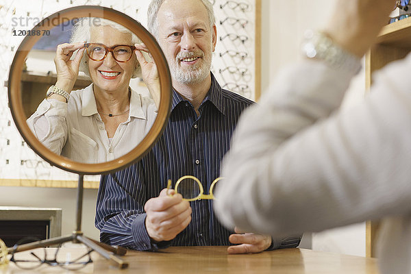Optikerin unterstützt lächelnde Frau bei der Brillenauswahl im Geschäft