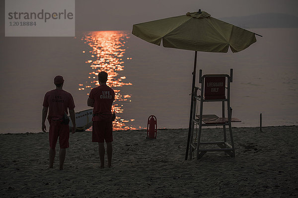 Rückansicht der am Strand stehenden Rettungsschwimmer bei Sonnenuntergang