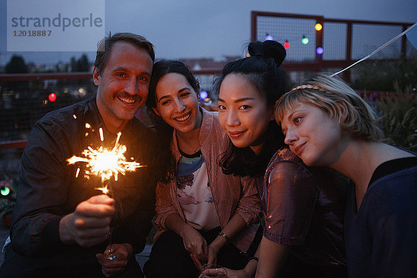 Porträt eines glücklichen Mannes mit Wunderkerze  der nachts mit Freundinnen zusammensitzt