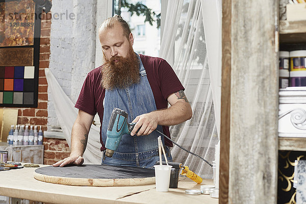 Mann trocknet Farbe auf Holz mit Trockner in der Werkstatt