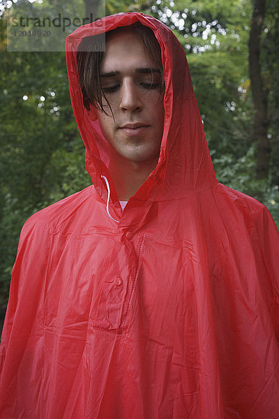 Nahaufnahme des jungen Mannes in rotem Regenmantel im Park