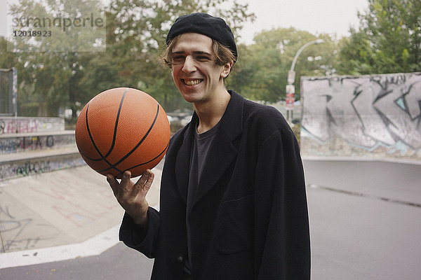 Fröhlicher junger Mann beim Basketballspielen im Park
