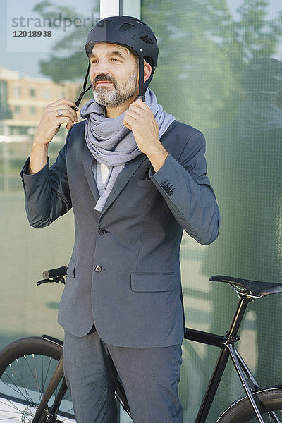Erwachsener Geschäftsmann mit Fahrradhelm im Stehen an der Glasscheibe