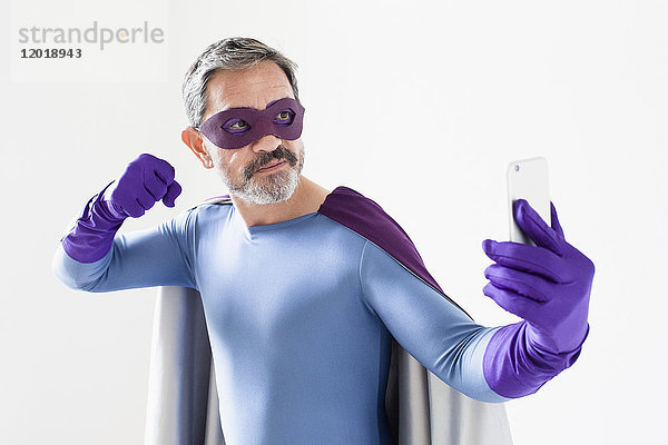 Superheld nimmt Selfie vom Smartphone  während er vor weißem Hintergrund steht.