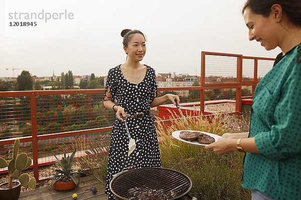 Lächelnde Frau serviert frisch gegrilltes Steak an Freundin auf der Terrasse