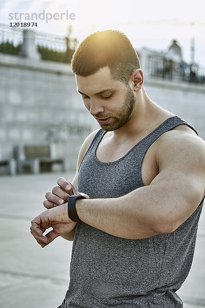Männlicher Sportler mit intelligenter Uhr im Stehen am Fußweg