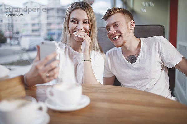 Glückliches junges Paar  das im Restaurant auf sein Handy schaut.