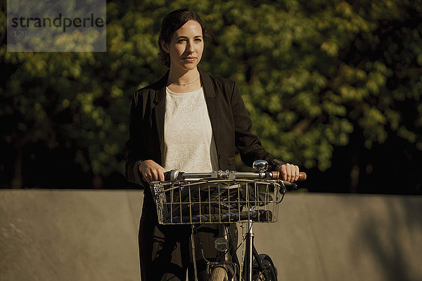 Nachdenkliche Geschäftsfrau stehend mit Fahrrad an sonnigen Tagen