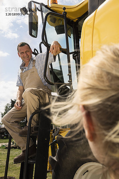Erwachsener Mann im Gespräch mit einer Frau  während er auf dem Traktor auf dem Bauernhof sitzt.