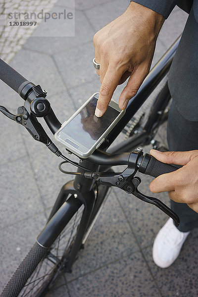 Beschnittenes Bild des Geschäftsmannes mit dem Handy am Fahrradgriff im Stehen auf der Straße