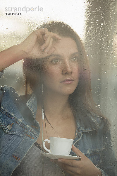 Nachdenklich schöne Frau mit Kaffeetasse beim Blick durchs Fenster