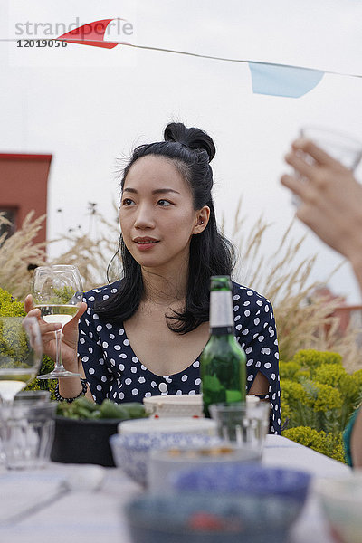 Nachdenkliche junge Frau mit Weinglas beim Sitzen am Außentisch während der Party