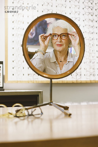 Porträt einer älteren Frau  die eine Brille trägt  die auf dem Spiegel im Geschäft reflektiert wird.
