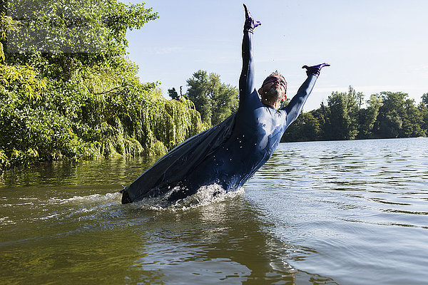 Reife Superhelden springen mit erhobenen Armen im Fluss gegen den Himmel