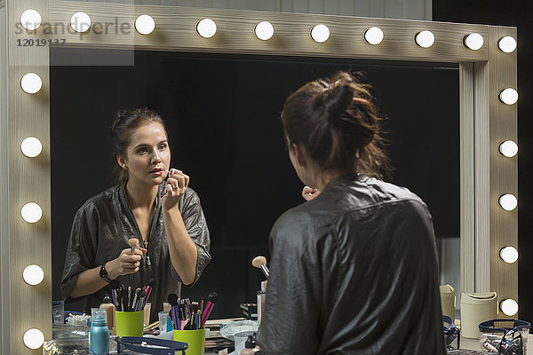 Schöne Frau mit Lipgloss vor dem Spiegel