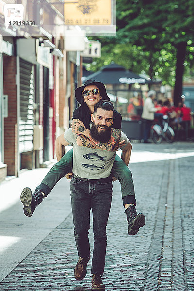 Junger Mann trägt seine Freundin auf dem Rücken in einer städtischen Umgebung