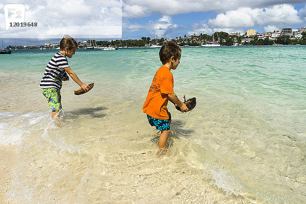 Zwei Jungen  5 und 7 Jahre alt  spielen mit einem kleinen Boot in Kokosnuss am Strand  Insel Gosier  Guadeloupe  Frankreich