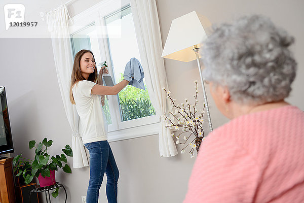 Fröhliches junges Mädchen  das einer älteren Frau zu Hause bei der Hausarbeit hilft.