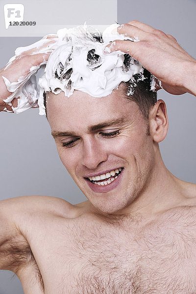 Oben-ohne-Mann  mit Shampoo in den Haaren  nach unten schauend  lächelnd  Haare waschend  mit Schaum auf dem Kopf
