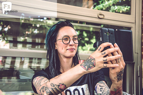 Porträt einer jungen Frau  die auf einer Restaurantterrasse sitzt und ein Selfie macht