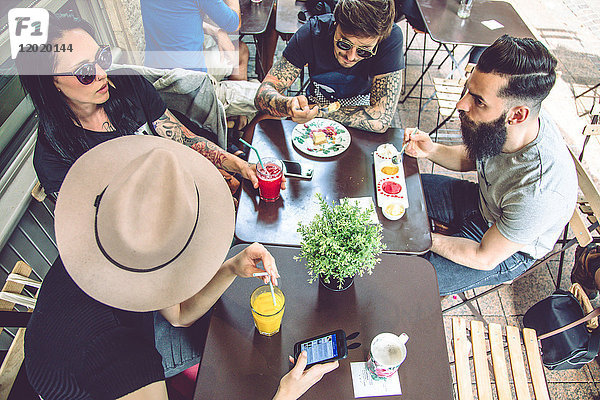 Gruppe junger Hipster  die auf einer Restaurantterrasse sitzen  essen und trinken