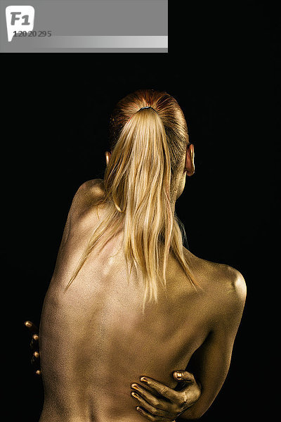 Porträt eines in Gold gemalten jungen Frauenkörpers  Rücken  Hände auf Quoten