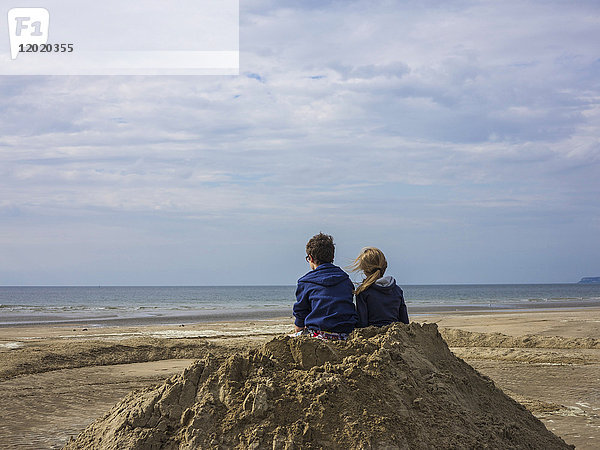Normandie  Zwei Kinder am Strand von hinten gesehen auf einem Sandhaufen
