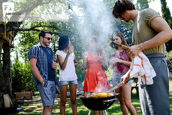 Eine Gruppe glücklicher und fröhlicher junger Leute  die sich während einer Sommerferienparty im Garten am Grill vergnügen.