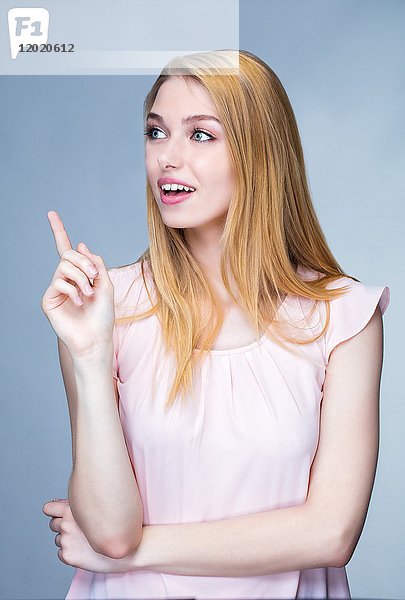 Porträt einer lächelnden jungen Frau mit erhobenem Finger an der Seite
