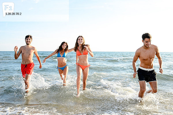 Frankreich  vier junge Erwachsene  die im Badeanzug im Meer laufen.