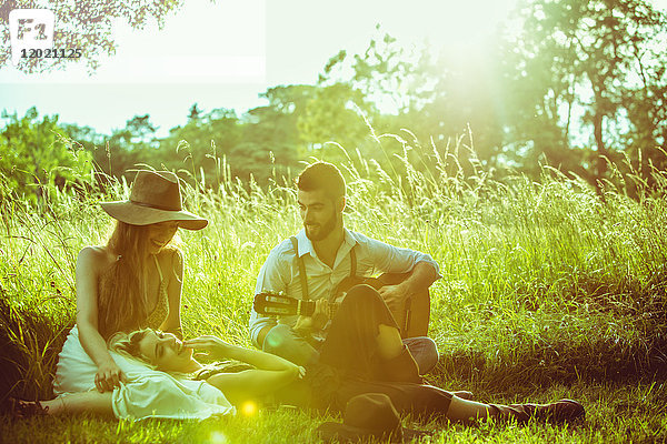 Gruppe von jungen Hipstern  die im Gras sitzen und Gitarre spielen