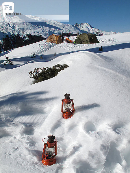 Österreich  Nordtirol Stubaier Alpen Fotschtal  2 Öllampen stehen im Neuschnee  während man im Hintergrund 2 große Campingzelte im Schnee mitten in den Bergen sieht