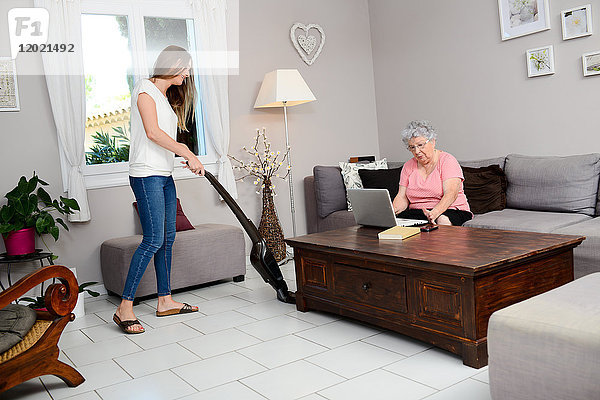 Fröhliches junges Mädchen  das einer älteren Frau zu Hause bei der Hausarbeit hilft.