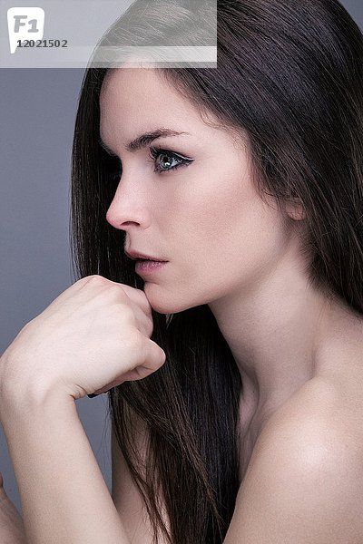 Porträt einer jungen Frau im Profil  Hand unter dem Kinn  Blick in die Linse