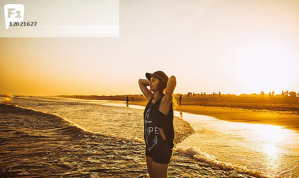 Junge Frau Hände hinter dem Kopf  halten das Meer am Strand Praia do Barril in einem Sonnenuntergang  deTavira Stadt  Region Algarve  Portugal