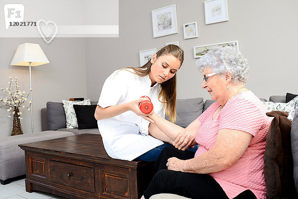 Junge Krankenschwester in der Physiotherapie hilft älteren Frauen bei der körperlichen Rehabilitation zu Hause