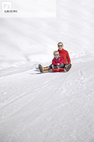 Porträt einer lächelnden Frau  die mit ihren Kindern auf einem Schlitten im Schnee sitzt  Crans-Montana  Schweizer Alpen  Schweiz.