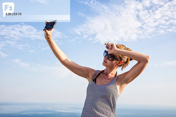 Porträt einer jungen Frau im Profil  die ein Selfie mit ihrem Smartphone auf den Höhen von Setubal  Lissabon und Umgebung  Portugal  macht